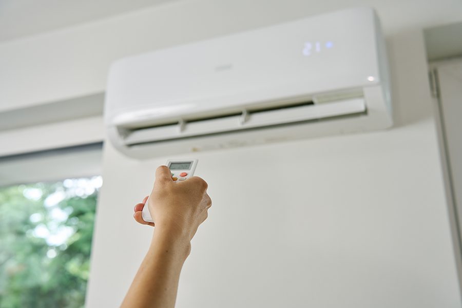 A person is holding a remote control, pointing it at a white air conditioning unit on a wall.