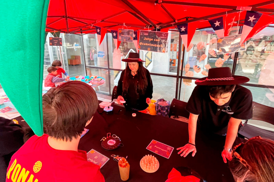 Estudiantes departen en una mesa con motivos patrios como banderas chilenas, sombreros negros y juegos