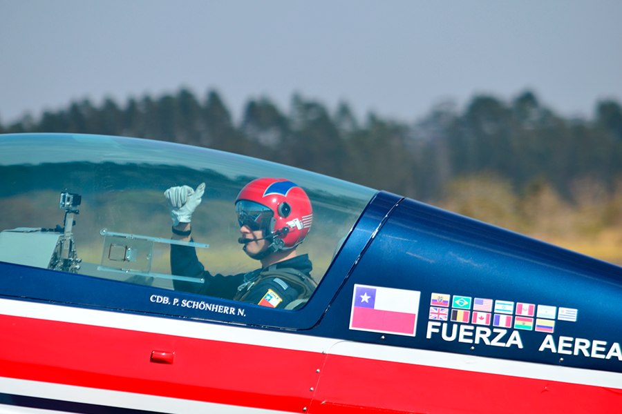 Toma de primer plano de un piloto desde la cabina de un avión azul y rojo, con la bandera chilena y la inscripción «FUERZA AÉREA» visibles en el fuselaje.