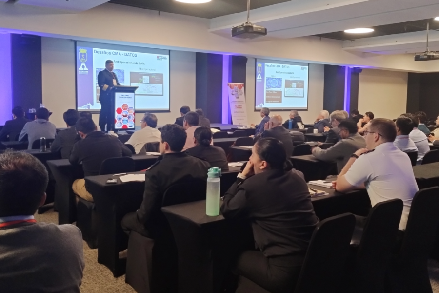 En la imagen aparece un investigador dando su conferencia frente a una interesada audiencia. La audiencia está sentada y el expositor de pie. De fondo luce su ppt.