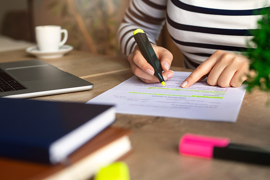 Una persona con una camisa a rayas se inclina sobre un escritorio para resaltar texto en un documento con un marcador amarillo fluorescente.