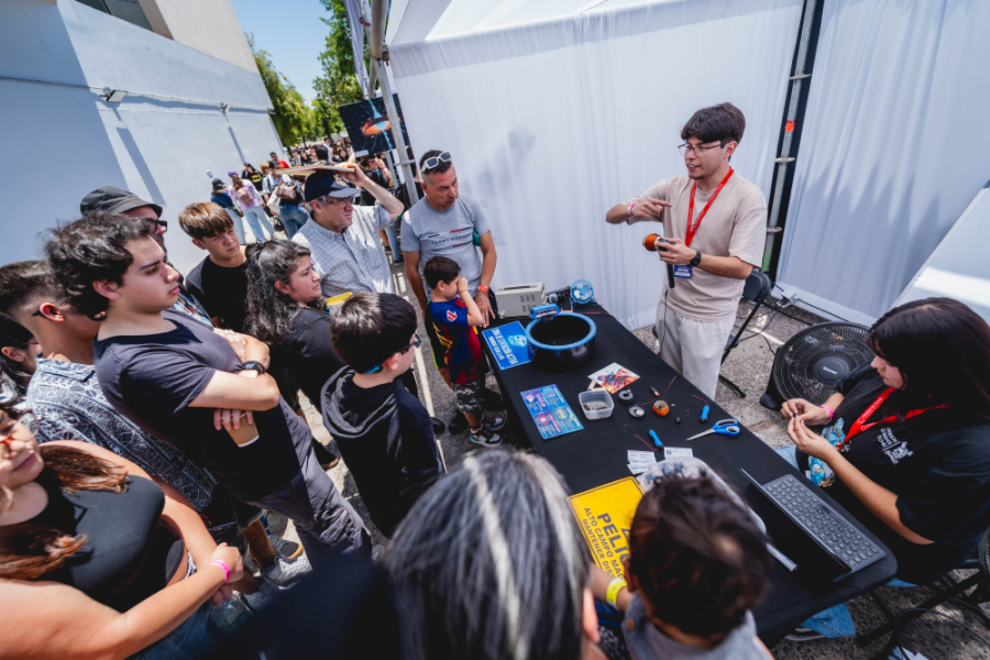 Niños y niñas observan interesados a los estudiantes de nuestra universidad que les enseñan de manera entretenida sobre ciencia y tecnología., en los patios de la Usach