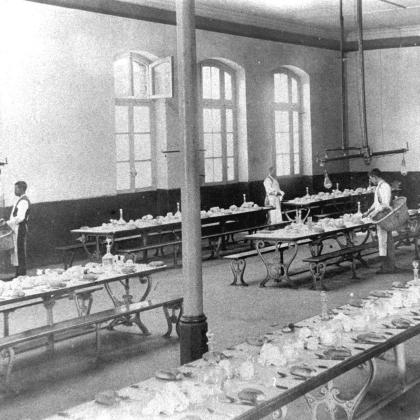 Vista de hombres disponiendo las mesas al interior del comedor para 300 alumnos de la Escuela de Artes y Oficios.