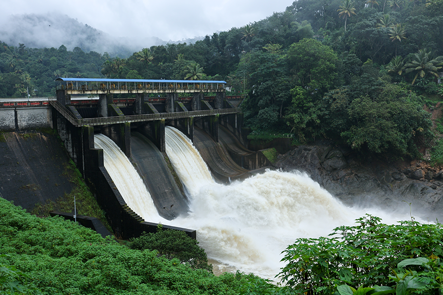 Una represa de hormigón en un bosque tropical tiene tres compuertas abiertas que liberan potentes cascadas de agua blanca hacia un río.