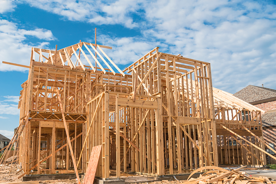 Wooden frame of a house under construction against a bright blue sky with scattered clouds, showcasing architectural progress.