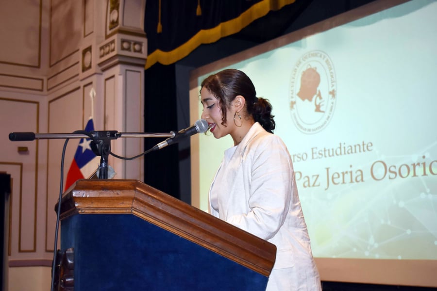 En la fotografía aparece una estudiante de la Facultad, realizando un discurso desde el podio del Teatro Aula Magna Usach