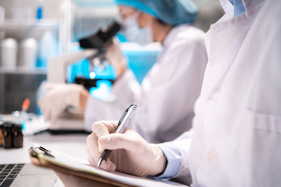 Científicos con batas blancas y gorras azules trabajan en un laboratorio, concentrados en los microscopios y tomando notas.
