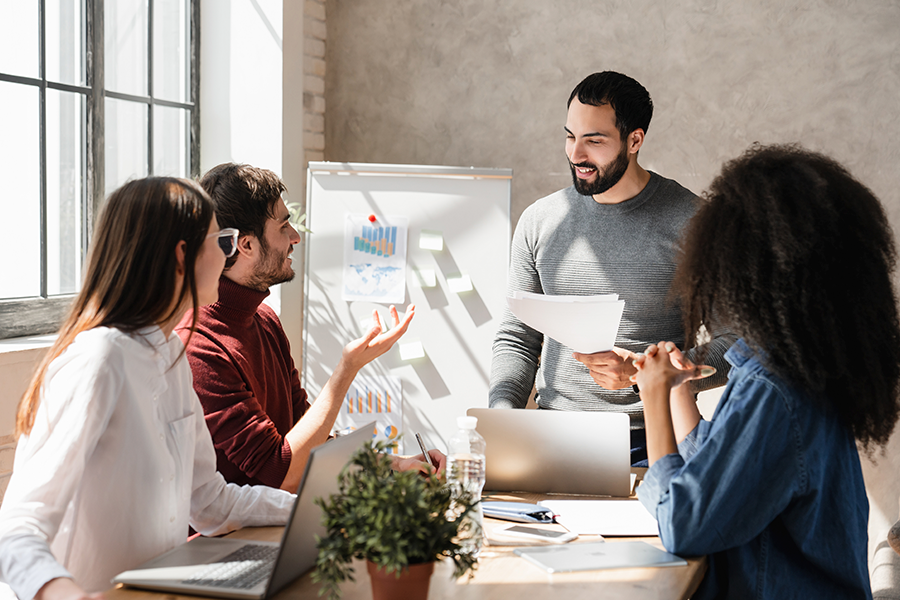 A diverse group of young professionals collaborates around a table in a bright, modern office space.