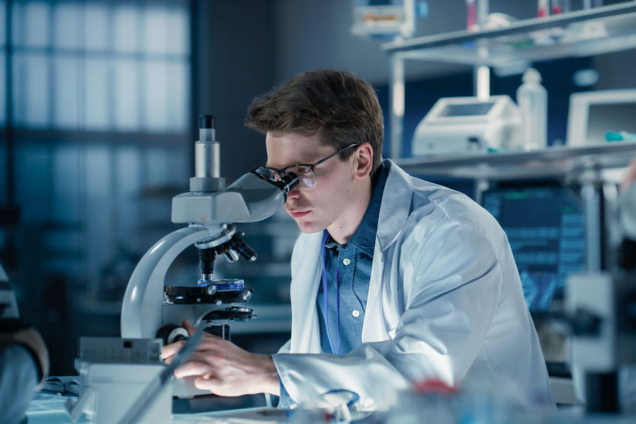 Un investigador con bata de laboratorio mirando a través de un microscopio.