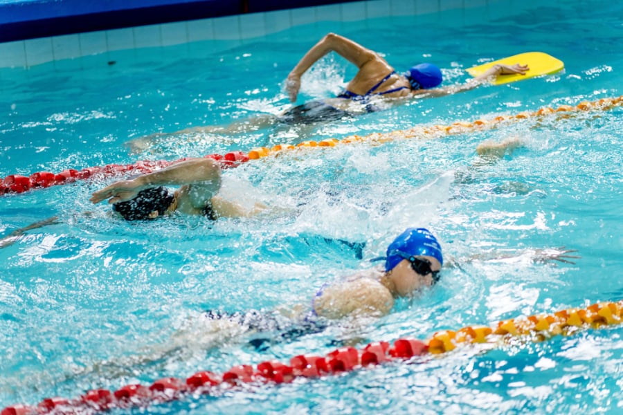 La imagen muestra tres personas practicando natación en la piscina de la universidad