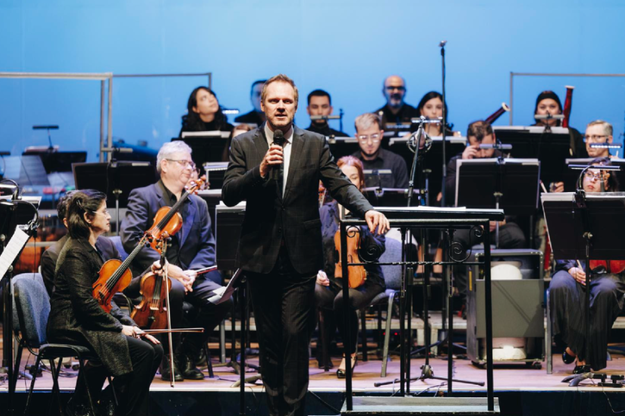 En la imagen aparecen una orquesta liderada por el director  Tobias Volkmann. El fondo del escenario es celeste.