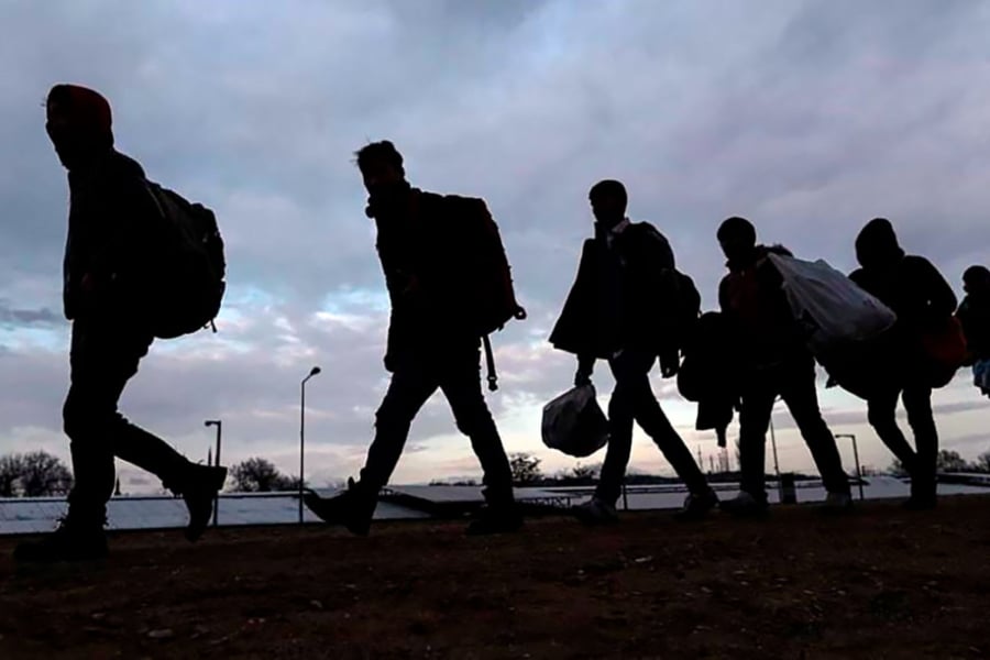 La imagen está a contraluz y muestra a cinco personas caminando en fila sosteniendo bolsas y pertenencias 