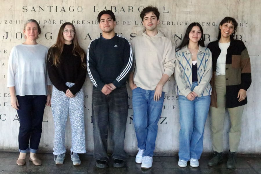 En la fotografía aparece 4 estudiantes de arquitectura, dos hombres, dos mujeres, más dos profesoras de la carrera. De fondo, el muro de entrada al a Rectoría Usach
