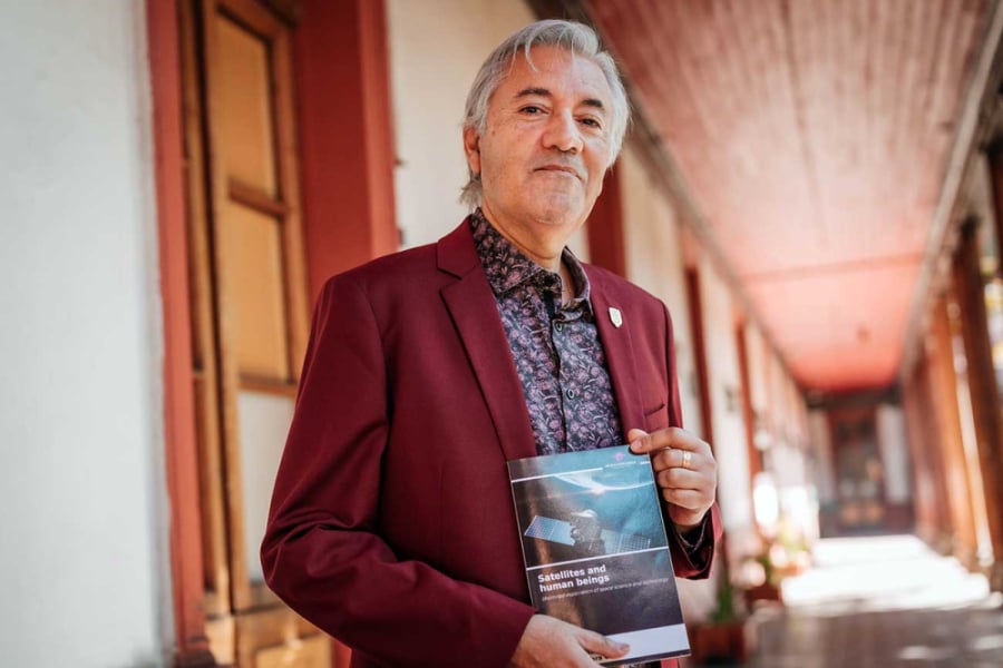 La imagen muestra al profesor con el libro en sus manos en un pasillo del edificio EAO
