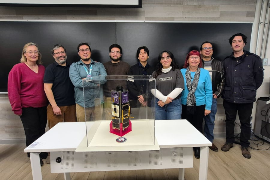 La imagen muestra a las y los participantes del proyecto posando frente al nanosatélite 