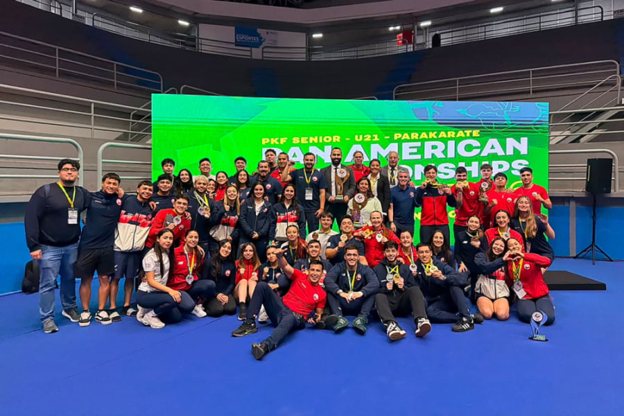 La imagen muestra al equipo completo de la selección chilena de karate posando con sus premios en el escenario principal del evento