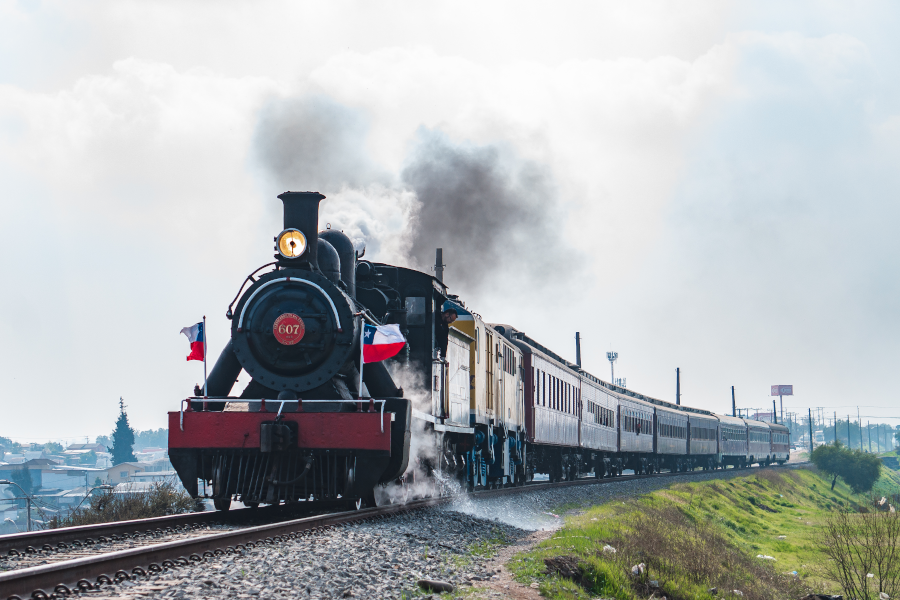 An antique steam locomotive with Chilean flags, moving along the tracks.
