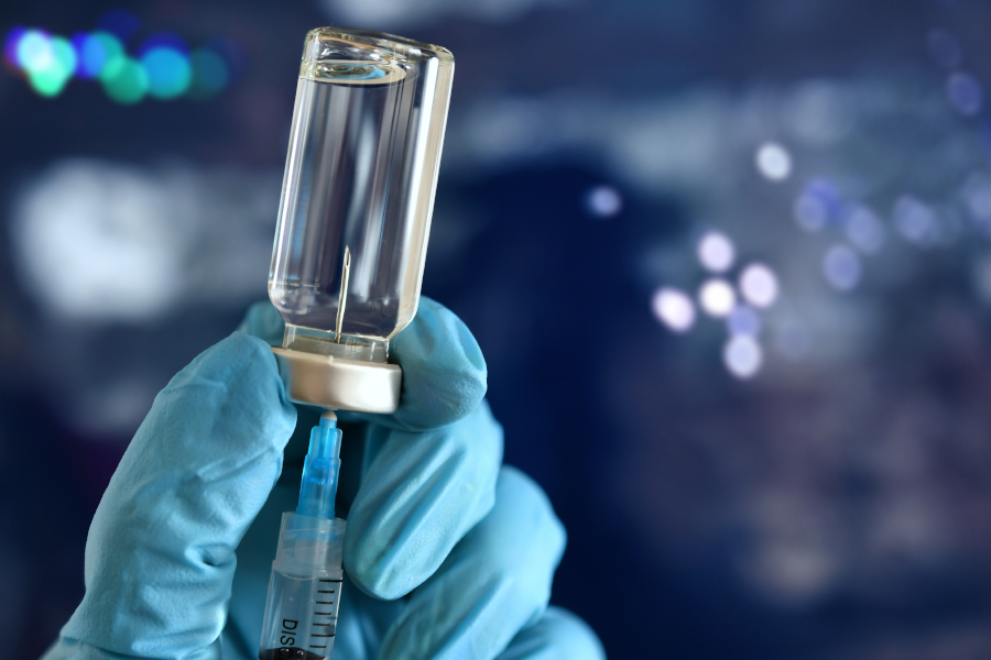 Gloved hand inserting a syringe needle into a medicine vial.
