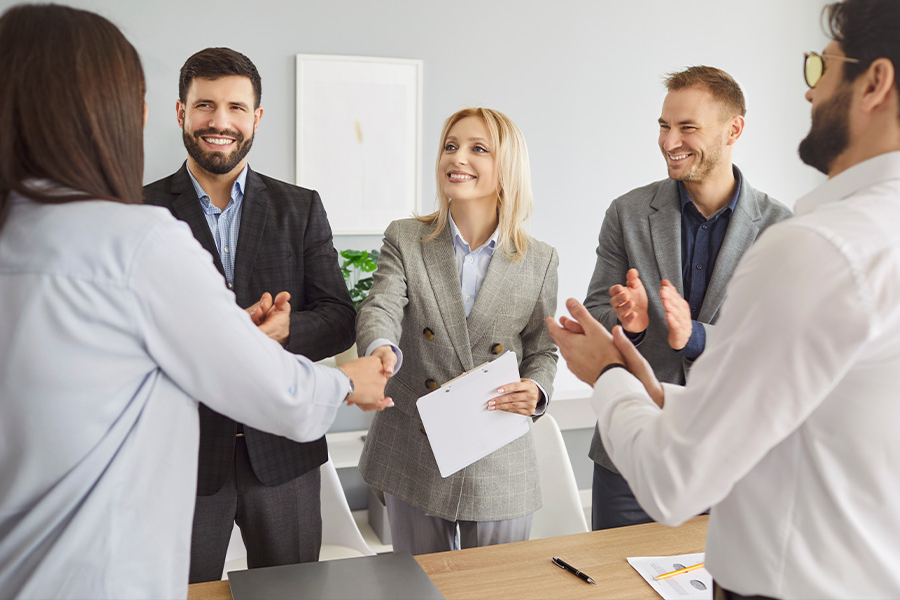 Empresarios dándose la mano y aplaudiendo alrededor de una mesa de reuniones.