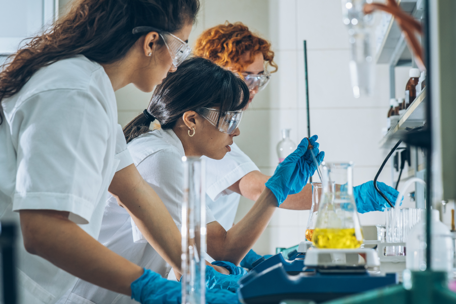 Three female scientists wearing glasses and gloves working in a lab.