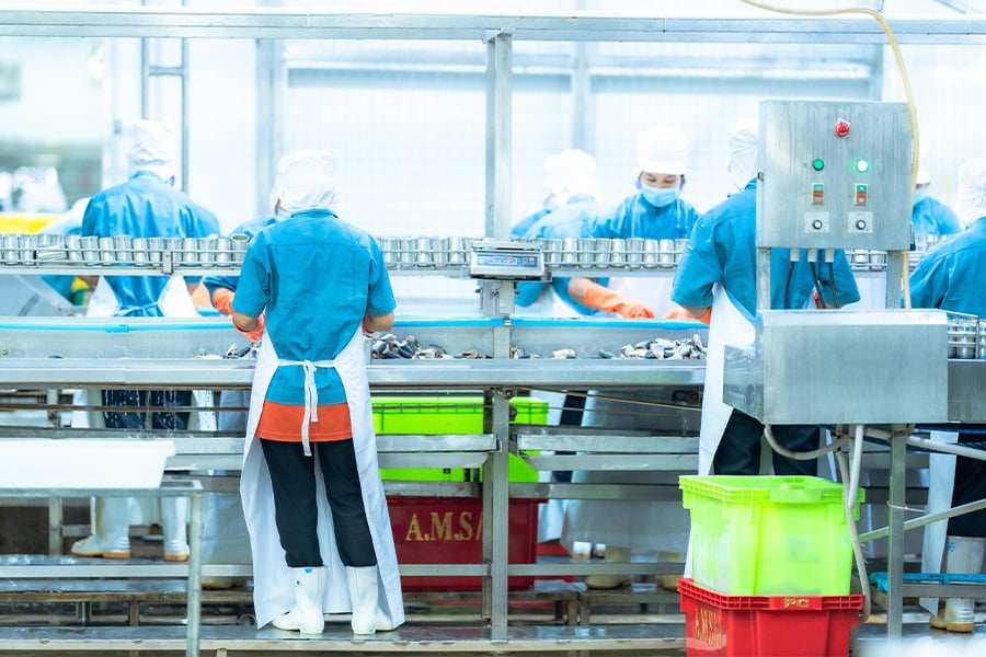 Factory workers in protective gear processing food on assembly line. 