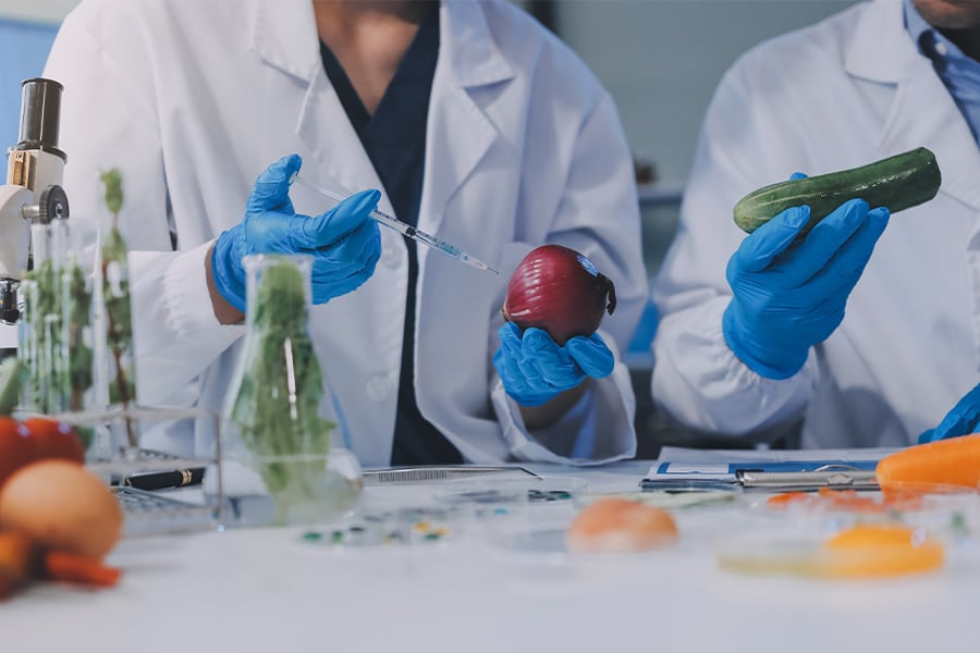 Científicos con batas de laboratorio analizando productos frescos con una jeringa.