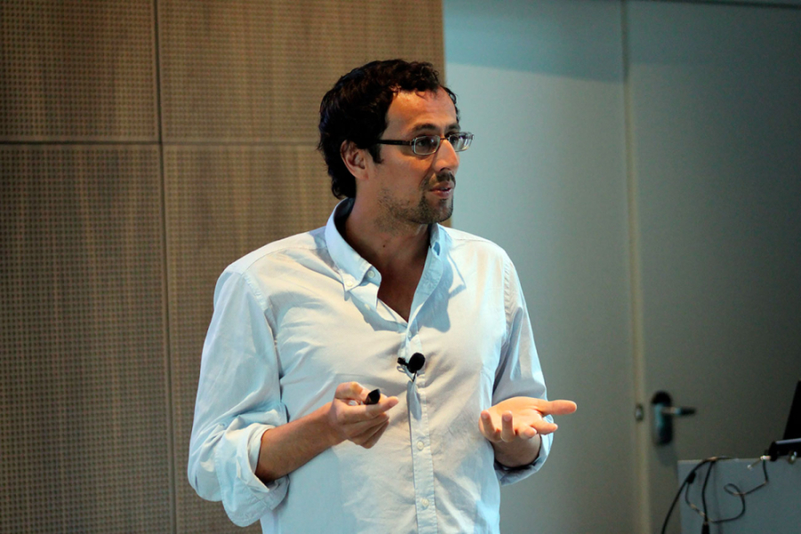 En la imagen aparece el Dr. Daniel Barrera, del Departamento de Matemática y Ciencia de la Computación (DMCC). El académico se dirige a la asistencia, Va vestido con camisa blanca.