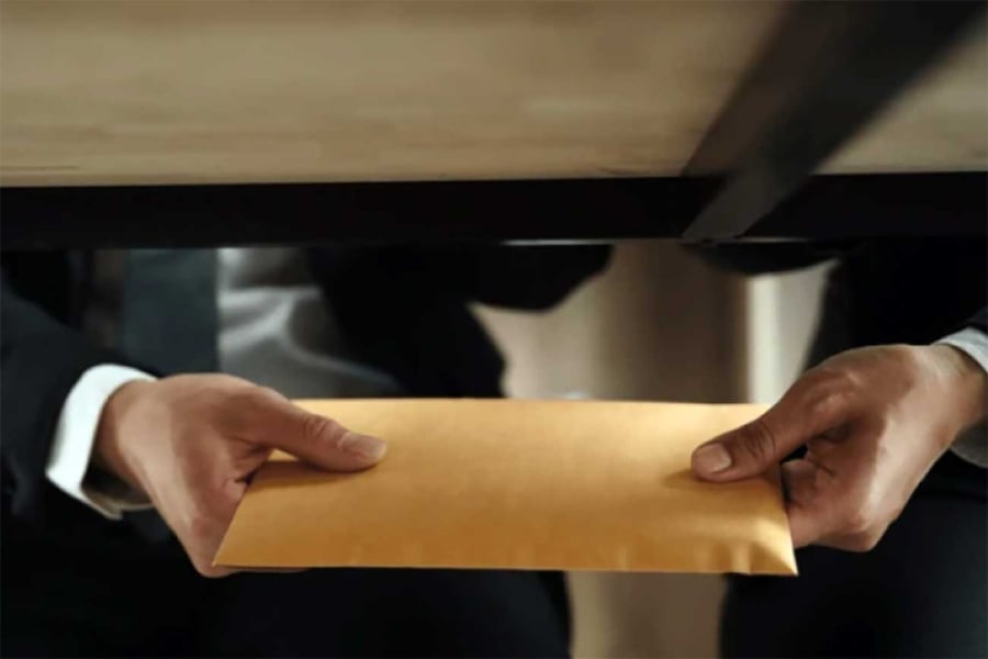 La imagen muestra un sobre amarillo debajo de una mesa siendo sostenido por dos manos