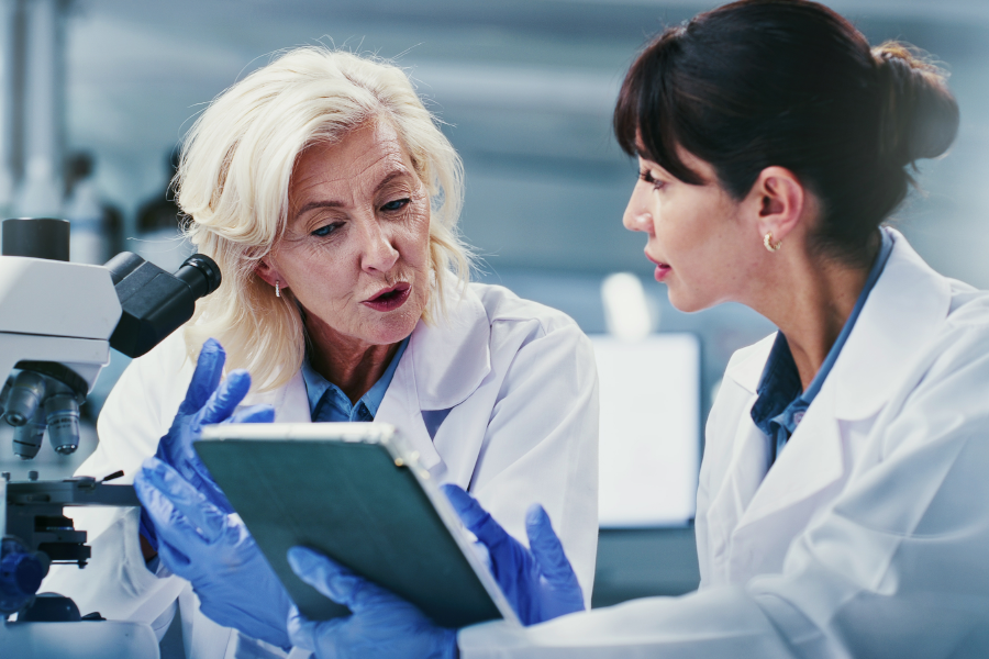 Dos científicos con batas de laboratorio discutiendo datos en una tablet.