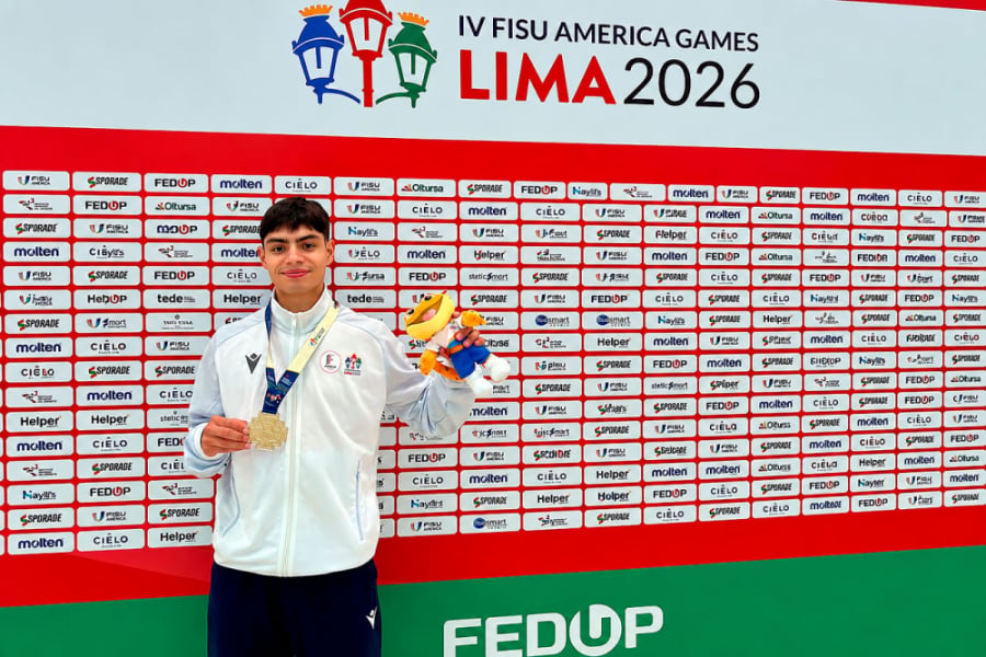En la fotografía aparece Víctor Jara, estudiante Usach quien logró una destacada actuación en FISU America Games 2026.. Aparece con una chaqueta de buzo blanca, una de sus medallas y la mascota del evento. De fondo, un panel con los sponsor del evento.