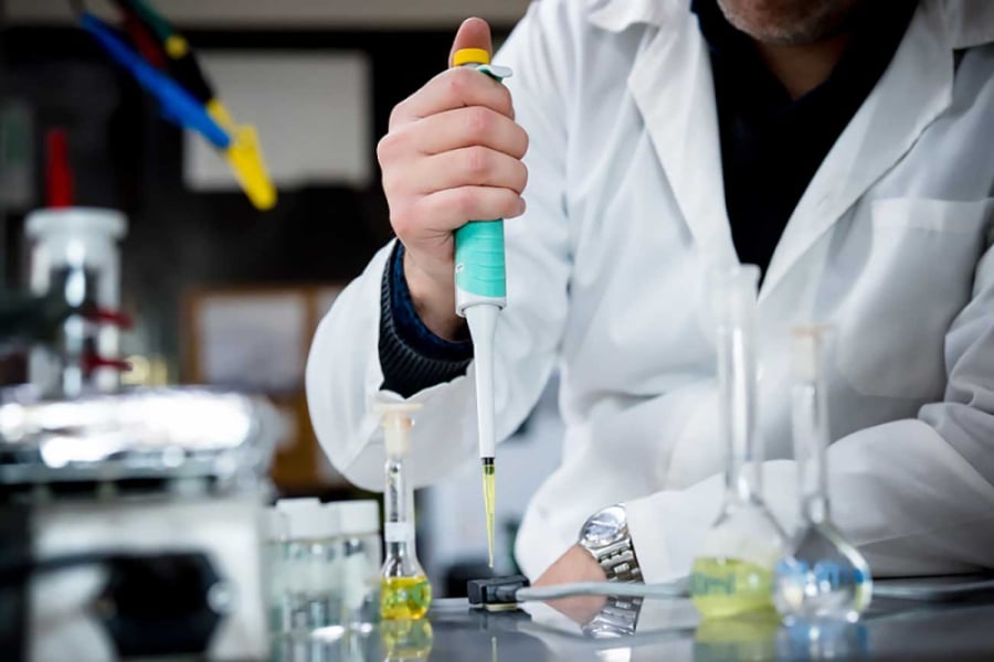 La imagen muestra una persona con bata blanca sosteniendo un utensilio en un laboratorio