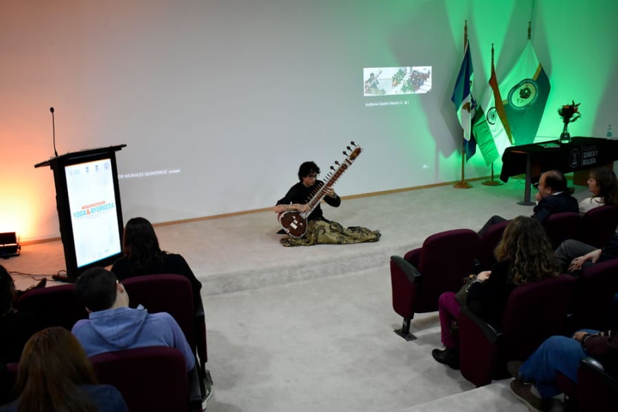 En la imagen aparece un músico tocando la cítara frente a parte de la comunidad estudiantil que llenó el Auditorio de la Facultad de Química y Biología