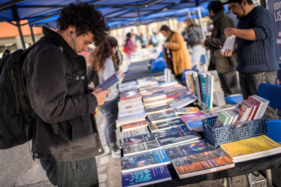 En la fotografía aparece una persona adquiriendo un libro en un stand de la Editorial Usach de su Librería Itinerante