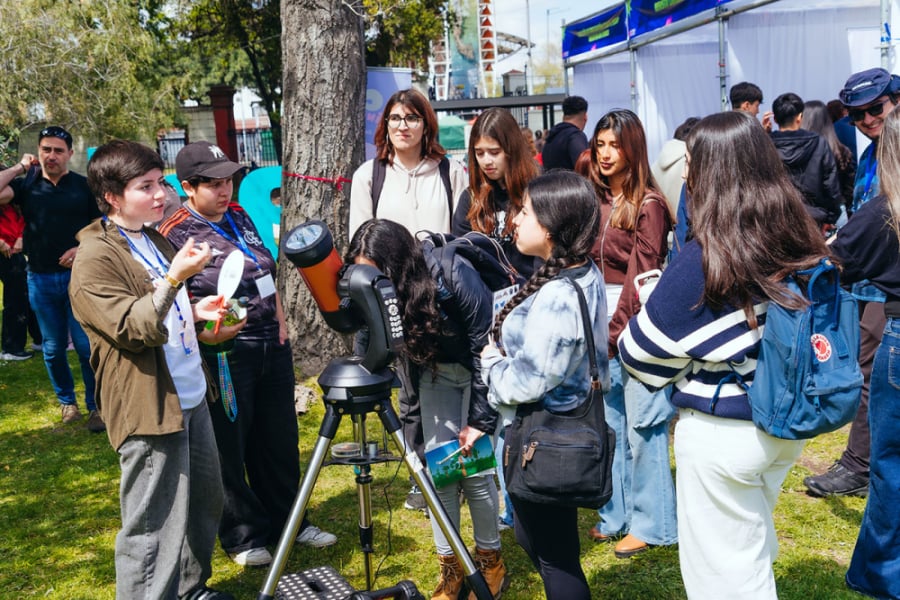En la imagen aparecen asistentes al evento alrededor de un telescopio. 